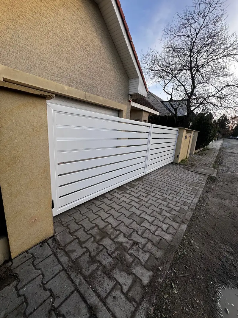 Biała brama przesuwna wzdłuż podjazdu z kostki, widok z boku