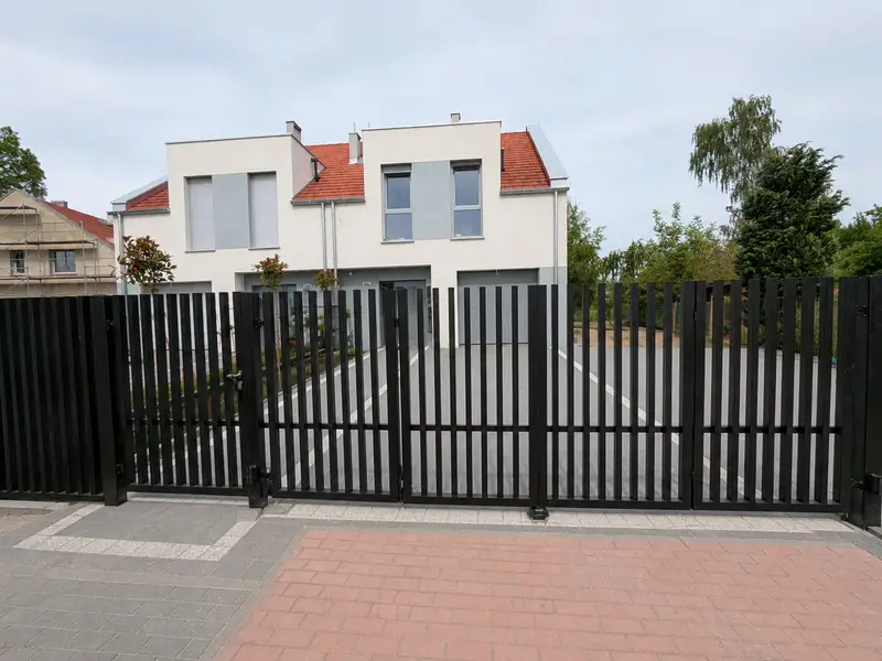 Czarna brama z pionowych profili przy podjeździe z czerwonej kostki