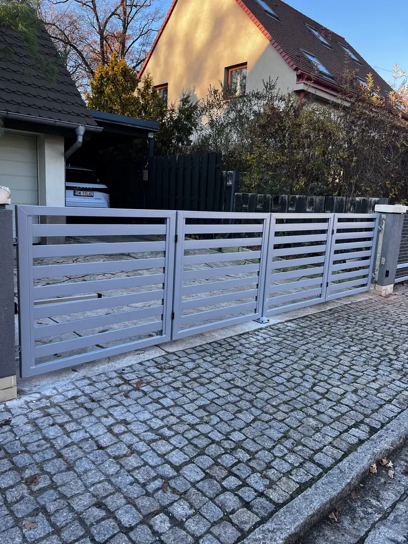 Srebrna brama dwuskrzydłowa z poziomych profili przed garażem