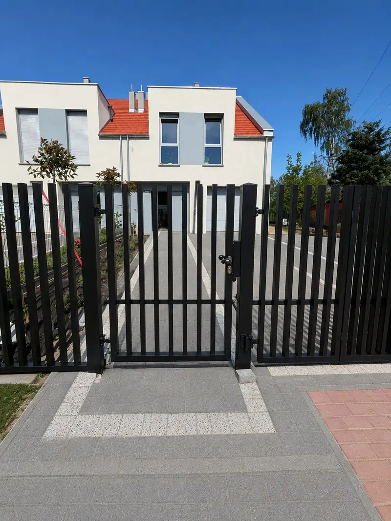 Czarna furtka z pionowych profili na wprost ścieżki do domu