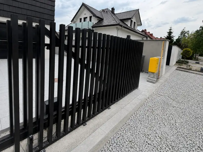 Czarne ogrodzenie z pionowych profili wzdłuż ulicy osiedlowej