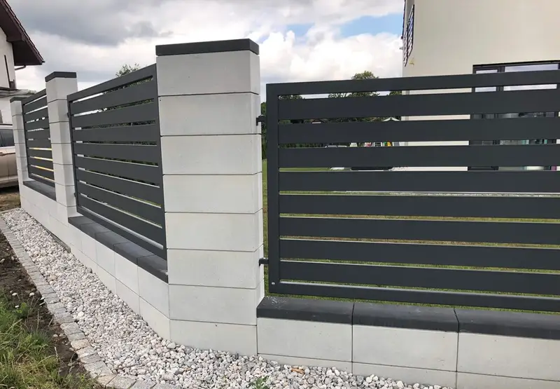 Ciemne poziome przęsła na jasnym murku z bloczków, widok wzdłuż ogrodzenia