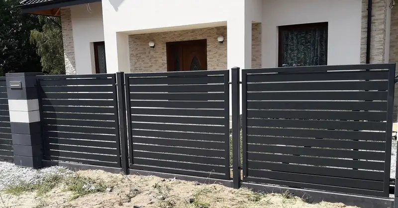 Grafitowe przęsła z poziomych profili przed wejściem do jasnego domu