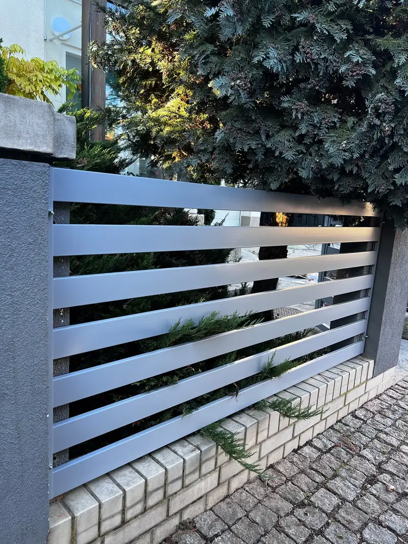 Srebrne przęsło z poziomych profili na murku z cegły klinkierowej