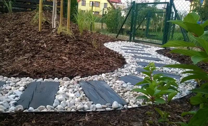 Łukowa ścieżka z białych otoczaków i ciemnych płyt wśród kory